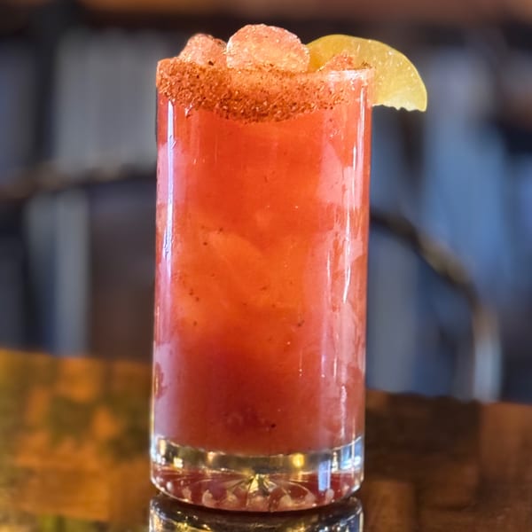 A vibrant red Mexican cocktail with a chili-lime rim, ice, and a lime wedge.
