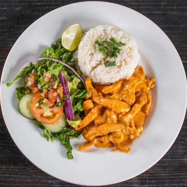 Casa Nueva's creamy chicken dish with white rice, fresh salad, and a lime wedge.