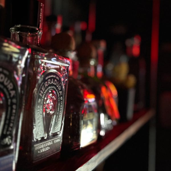 Close-up of Herradura tequila bottles on a dimly lit bar shelf with red accents.