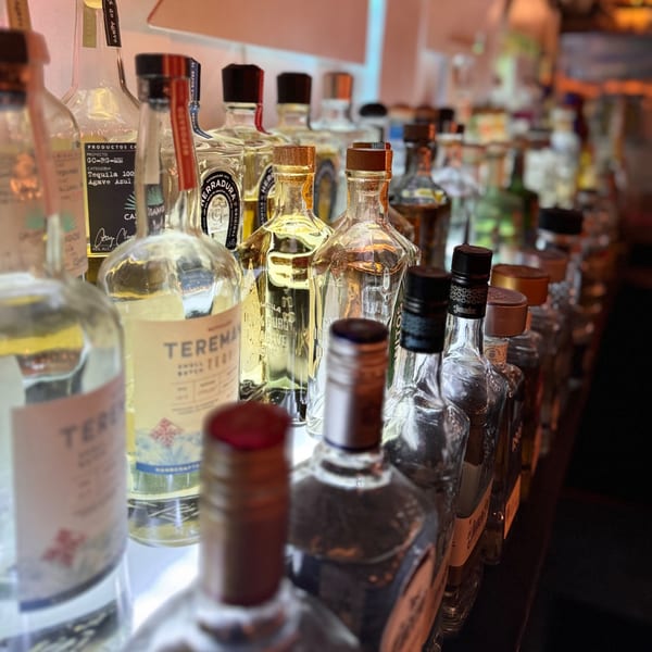 A close-up of various tequila bottles, including Teremana and Herradura, lined up on a bar shelf.