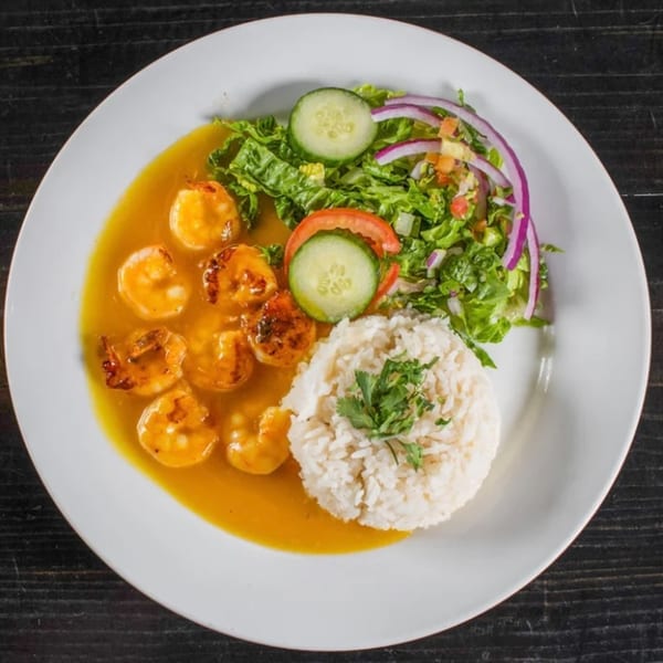 Casa Nueva's shrimp dish with yellow sauce, white rice, and a fresh salad with cucumbers and red onions.