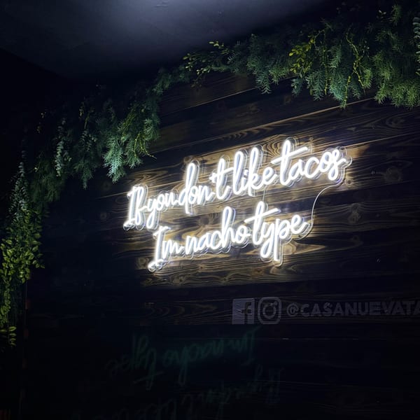 Neon sign on a dark wooden wall reads: "If you don't like tacos, I'm nacho type".