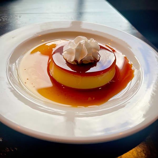 A flan dessert with caramel sauce and whipped cream on a white plate.