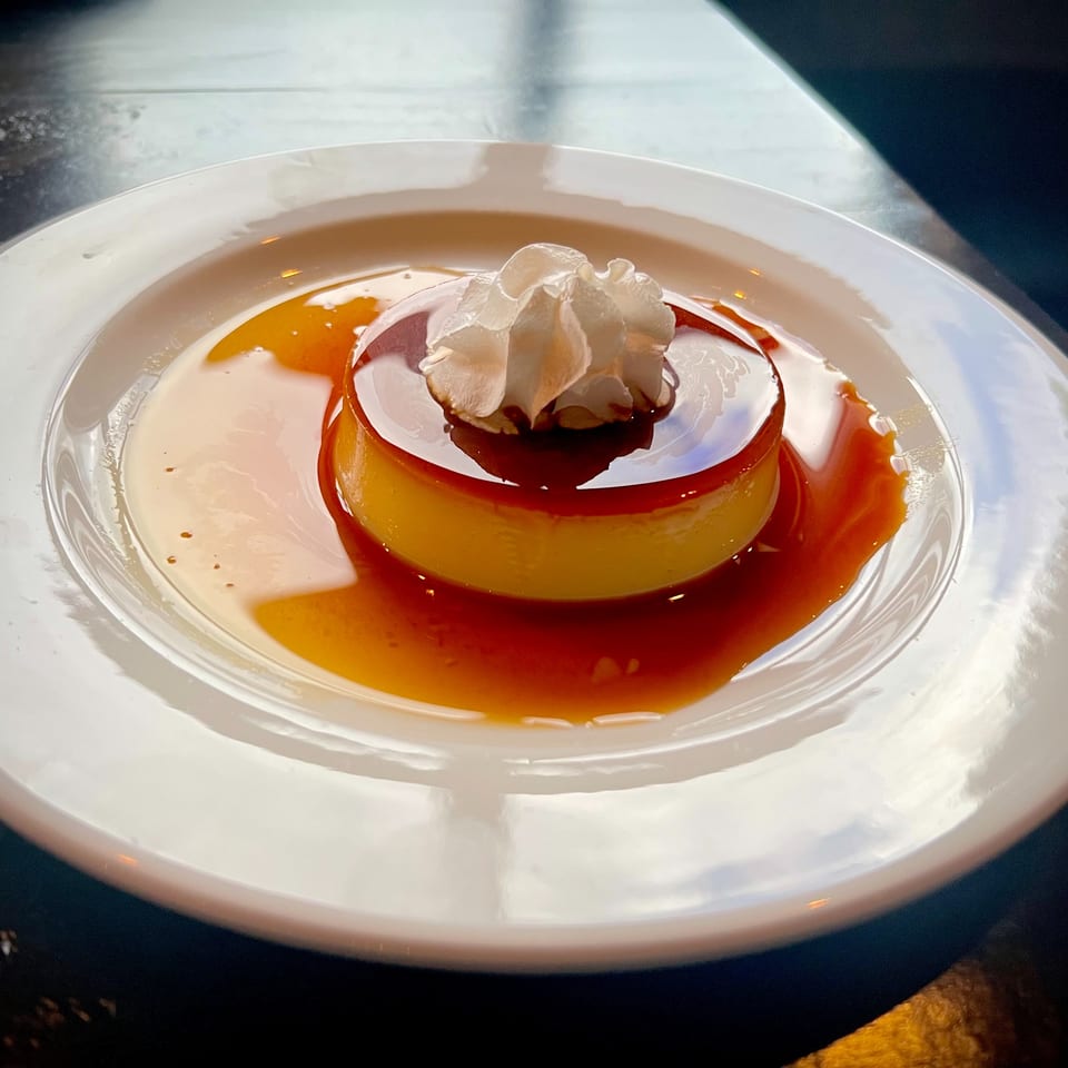 A flan dessert with caramel sauce and whipped cream on a white plate.