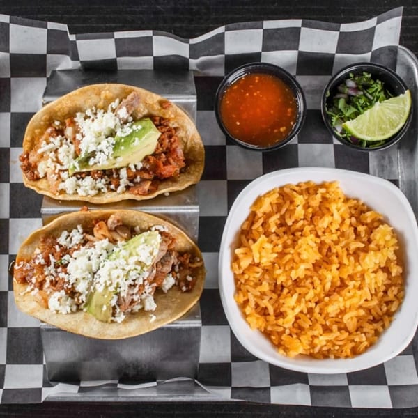 Two Casa Nueva tacos with rice, salsa, and cilantro with lime on a checkered paper.