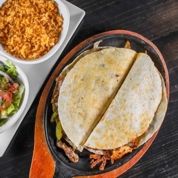 Sizzling fajita quesadilla with rice and salad, served on a black wooden table at Casa Nueva.
